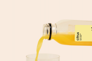 Citrus cold-pressed juice being poured into a glass, showcasing vibrant orange color and freshness.