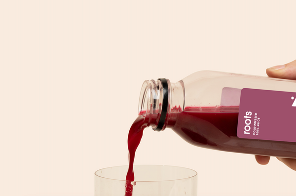 Roots Cold-pressed Juice being poured into a glass, showcasing vibrant beet and carrot blend.